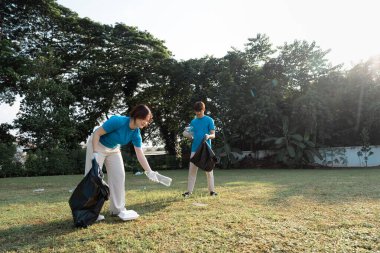 Toplumun temizlik etkinliği sırasında çöpleri ve plastik atıkları özenle toplayarak çevresel farkındalığı artıran uyumlu mavi gömlekler içinde hevesli iki gönüllü..