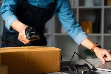 Girişimci, çevrimiçi siparişler için paketleri tarar, modern bir çalışma alanında etkili envanter yönetim uygulamaları gösterir.