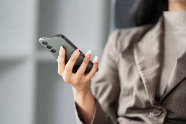 Genç profesyonel bir kadın, modern ofis alanındaki teknoloji ve işi harmanlayan akıllı telefonunu kontrol eder..