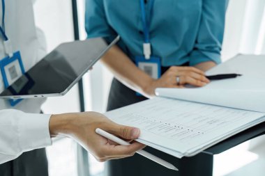 Şirket ortamında takım çalışması ve etkili iletişimi gösteren iki profesyonel belge ve tablet gözden geçirir.