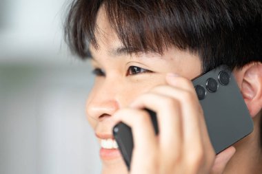 Genç bir adam, neşeli bir gülümseme ve nişanlı bir ifade sergileyerek telefonda konuşmaktan hoşlanır..