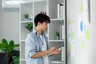 Odaklanmış genç bir profesyonel çizelgeleri değerlendirir ve notlar alır, iş analizi ve stratejisine olan bağlılığını gösterir.