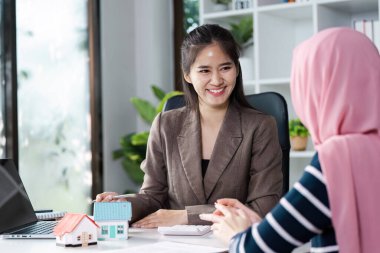 Çeşitli emlakçılar müşterilerine gülümsüyor ve onlarla yakınlaşıyor. Parlak ve modern ofis ortamında çeşitli model evleri tartışıyorlar..