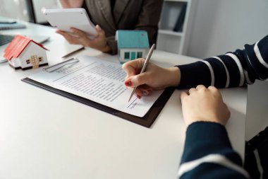 Bir müşteri, model evlerle çevrili bir menajerin yardımıyla emlak sözleşmesi imzalıyor..