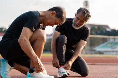 İki son sınıf öğrencisi, ayakkabı bağcıklarını piste bağlayıp sağlıklı yaşam ve aktif yaşam koşullarını vurgulayarak antrenmana hazırlanıyor..