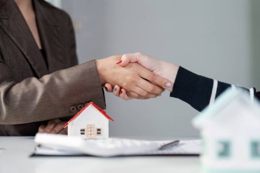 Bir emlakçı ve müvekkil, sözleşme imzaladıktan sonra model evlerle el sıkışıyor..