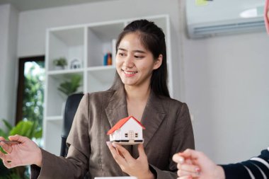Profesyonel bir emlakçı, elinde bir model ev tutarken müşteriyle mülkiyet seçenekleri hakkında tartışırken gülümser..
