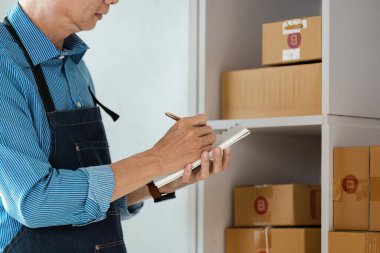 Odaklanmış bir e-ticaret şirketi sahibi, çevrimiçi satışlar ve lojistiğin etkin yönetimini vurgulayarak, ev ofisinde envanter ayrıntılarını kaydeder..