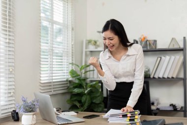 Memnun bir kadın muhasebeci, modern ofis ortamında evrak işleriyle çevrili bir yumrukla neşeyi ifade eder..