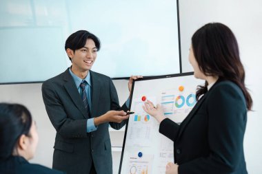 Meslektaşlarına finansal veriler sunan bir iş adamı, çağdaş bir ofis ortamında katılım ve işbirliğini teşvik eder.