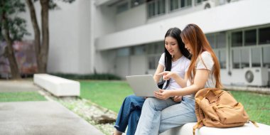 İki üniversite öğrencisi açık havada bir dizüstü bilgisayarda birlikte çalışarak, işbirlikçi bir öğrenme ortamı oluşturuyorlar..