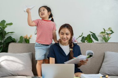 Neşeli bir çocuk kağıttan bir uçakla oynarken, annesi evrak işleriyle uğraşıyor, aile nişanının keyfini vurguluyor..
