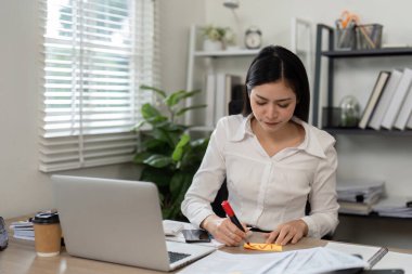 Odaklanmış bir kadın muhasebeci finansal belgeler üzerine notlar yazar, profesyonel bir ortamda örgütsel becerilerini gösterir..