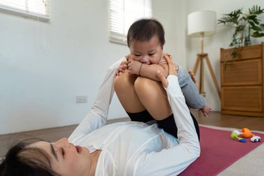Bir annenin bebeğiyle yoga yaptığı neşeli bir an. Huzurlu bir ev ortamında iyileşme ve bağlanma..