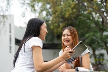 İki öğrenci çalışmalarını canlı bir şekilde tartışır, güneşli bir ortamda fikir alışverişinde bulunur ve gülümserler..