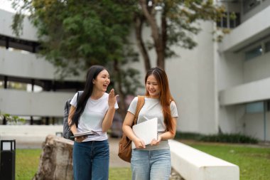 Kampüste yan yana yürüyen iki neşeli öğrenci ödevleri hakkında sohbet ediyorlar..