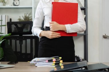 Bir iş adamı, kurumsal bir ortamda önemli belgelerin yönetimini ve organizasyonunu sembolize eden kırmızı bir klasöre sahiptir..