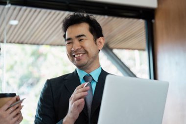 Neşeli bir iş adamı, bir iş arkadaşı ile bir dizüstü bilgisayar üzerinde çalışırken, iş yerinde işbirliği ve pozitiflik gösterirken etkileşime girer..