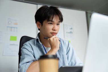 Kendini işine adamış genç bir adam modern bir çalışma alanında stratejiler düşünüyor, iş analizindeki konsantrasyon ve verimliliği vurguluyor..