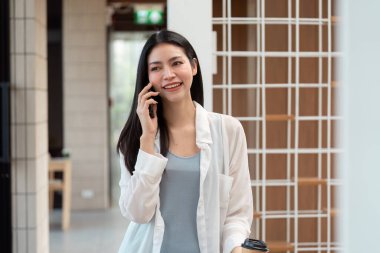 Bir kadın elinde bir fincan kahveyle bir telefon görüşmesi yapar. Günümüz dünyasında sürdürülebilir yaşam ve etkili iletişim arasındaki sinerjiyi temsil eder..