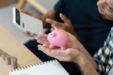 Bir LGBTQ çifti birikimlerini bir kumbara ve hesap makinesi kullanarak birlikte mali geleceklerini planlarken inceliyor..