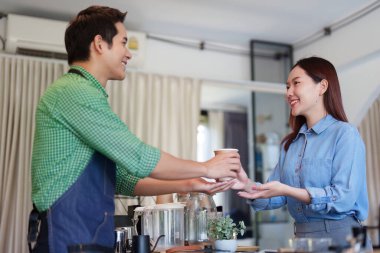 Sürdürülebilir bir kafede dostça bir değiş tokuş. Kahveci, kahve bardağını keyifli bir müşteriye uzatıyor. Bu da çevreci dostluğa olan bağlılığını yansıtıyor..