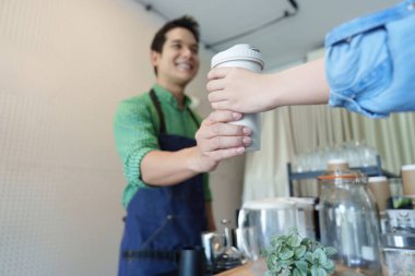 Dost canlısı bir barista, yeniden kullanılabilir bir kahve fincanını müşterisine verirken gülümsüyor ve kafenin sürdürülebilirlik ve yerel toplum sözleşmesine olan bağlılığını vurguluyor..
