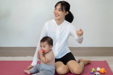 Fitness rutininin ortasında, bu anne neşeyle ebeveynliği kucaklıyor, yanında renkli bir minder üzerinde oynayan bebeğiyle meşgul oluyor..