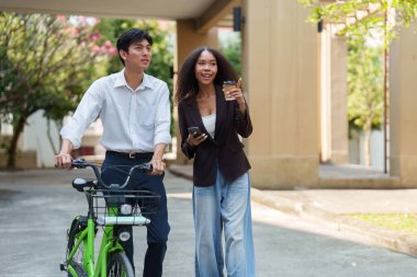 Genç bir adam, kahve yudumlayan ve telefonunu kaydıran bir kadınla birlikte bisiklete biniyor. Sürdürülebilirlik ve sosyal etkileşime odaklı bir yaşam tarzını temsil ediyor..