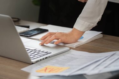 Vergi dosyalarının karmaşıklığını ve etkili belge yönetiminin önemini gösteren belgelerle dolu bir masanın üzerinde vergi evraklarını düzenleyen bir el görülüyor.
