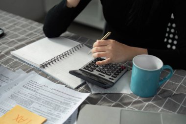 Bir birey, vergi hazırlama ve yönetim sürecinin eksiksiz bir şekilde gösterildiği önemli vergi rakamlarını bir deftere kaydederken, önemli vergi rakamlarını hesaplar..