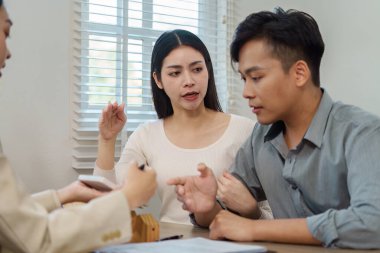 Bir emlakçı müşterilerle yakınlaşır, mülkiyet detaylarını ve seçenekleri parlak ofis ortamında tartışır..