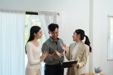 Parlak bir odada, iki müşteri bir emlakçıyla iletişim kurar, karşılıklı bağlılık ve ev seçenekleri hakkında heyecan gösterirler..