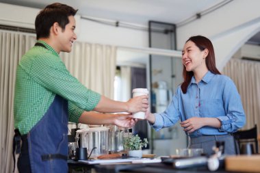 Kahveci, gülümseyen bir müşteriye sıcak bir kafe ortamında sürdürülebilir uygulamalara olan bağlılığını gösteren dumanı tüten bir fincan kahve verir..