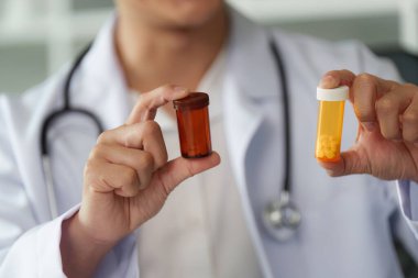 Bir doktor konsültasyon sırasında çeşitli ilaç konteynırları gösterir, seçenekleri vurgular ve bir hastayla tedavi planlarını tartışır,.