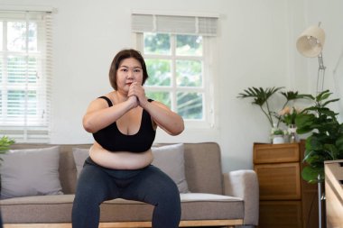 Kararlı bir duruşla, bu kadın oturma odasındaki çömelmelerle güç toplamaya odaklanıyor, sağlığına ve sağlığına olan bağlılığını gösteriyor..