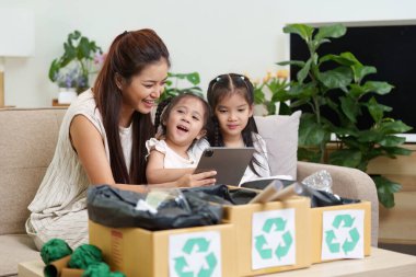 Bir anne ve çocuklarının geri dönüşüm aktivitesine girişip sürdürülebilirliği desteklemek için takım çalışmasının önemini vurguladıkları neşeli bir an..