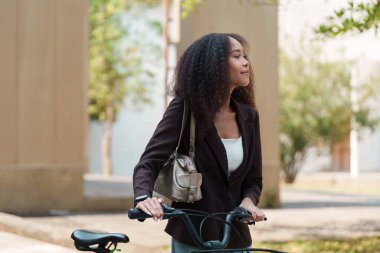Şık bir kadın bisikletiyle durur, sürdürülebilir ulaşımı kucaklayarak çevre dostu seyahat seçeneklerini seçer ve çantasını tutar..