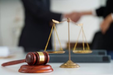 İki avukat el sıkışırken ön planda bir tokmak ve terazi müzakerelerin sonucunu ve hukukun otoritesini sembolize ediyor..