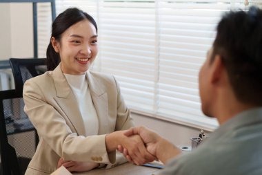 Profesyonel bir emlakçı bir müşteriyle görüşür, el sıkışır ve başarılı sonuçlar elde etmek için ev satışı stratejilerini tartışır..