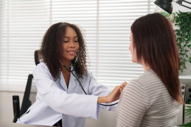 Dost canlısı bir doktor, steteskop kullanarak hastanın kalbini dinler ve rahat ve güvenilir bir ortam sağlar..