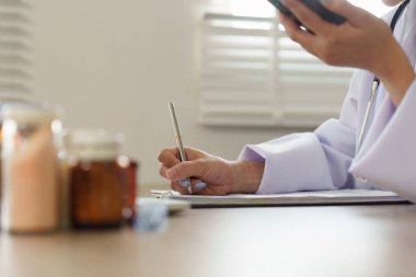 Bir doktor, tele sağlık randevusundaki önemli ayrıntıları not ederken, hasta bakımına teknolojinin entegrasyonunu gösteren bir akıllı telefon tutar..