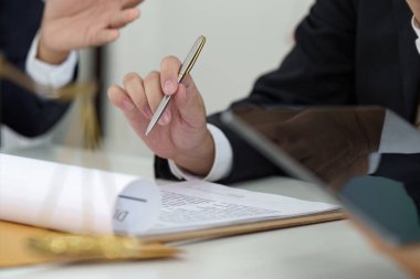 Bir avukat, müvekkiline kontrat imzalarken yol göstermeye hazır bir kalem tutar. Formaliteden önce tüm detayların net bir şekilde anlaşılmasını sağlar..