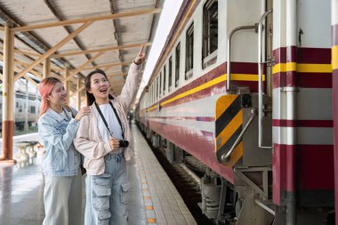 Platformda duran iki arkadaş, yolculuklarına çıkmanın heyecanıyla birlikte treni işaret ederek, keşif ve dostluğun özünü yakalıyorlar..