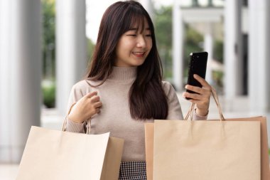 Mutlu bir kadın alışverişini sürdürülebilir alışveriş çılgınlığından sonra, modern tüketici alışkanlıklarını ve ekolojik bilinçli tercihleri yansıtarak, telefonundan değerlendiriyor..