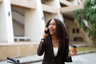 Genç kadın telefonuyla konuşurken zevk veriyor, şehir manzarası arasında sürdürülebilir bir yaşam tarzıyla sosyal bağlantıyı birleştiriyor..