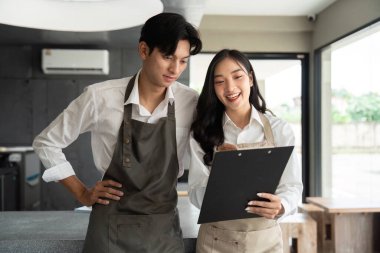 İki genç girişimci proje listelerini inceleyerek, stratejileri tartışıyor ve bir kafe ortamında küçük başarıları kutluyor, pozitif enerjiyi yansıtıyor.