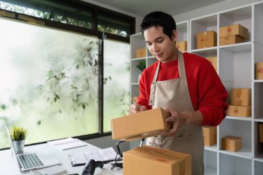 Parlak bir çalışma alanında, bu girişimci sevkiyattan önce kaliteyi sağlamak için paketleri kontrol eder, e-ticarette detaylara dikkat etmenin önemini vurgular.
