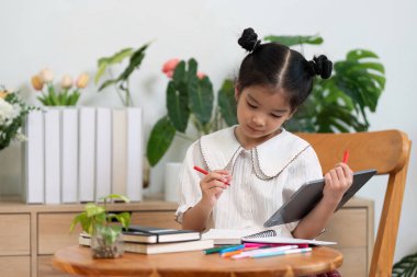 Odaklanmış bir kız çalışma masasında otururken okul malzemelerini kullanır, yaratıcılığı ve öğrenme ruhunu somutlaştırır..