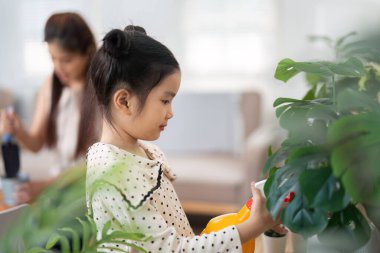 Yeşillik dolu parlak bir odada, bir kız bitkilerini dikkatlice annesinin rehberliğiyle suluyor, doğayı yetiştirmenin ve aile bağı kurmanın önemini vurguluyor..